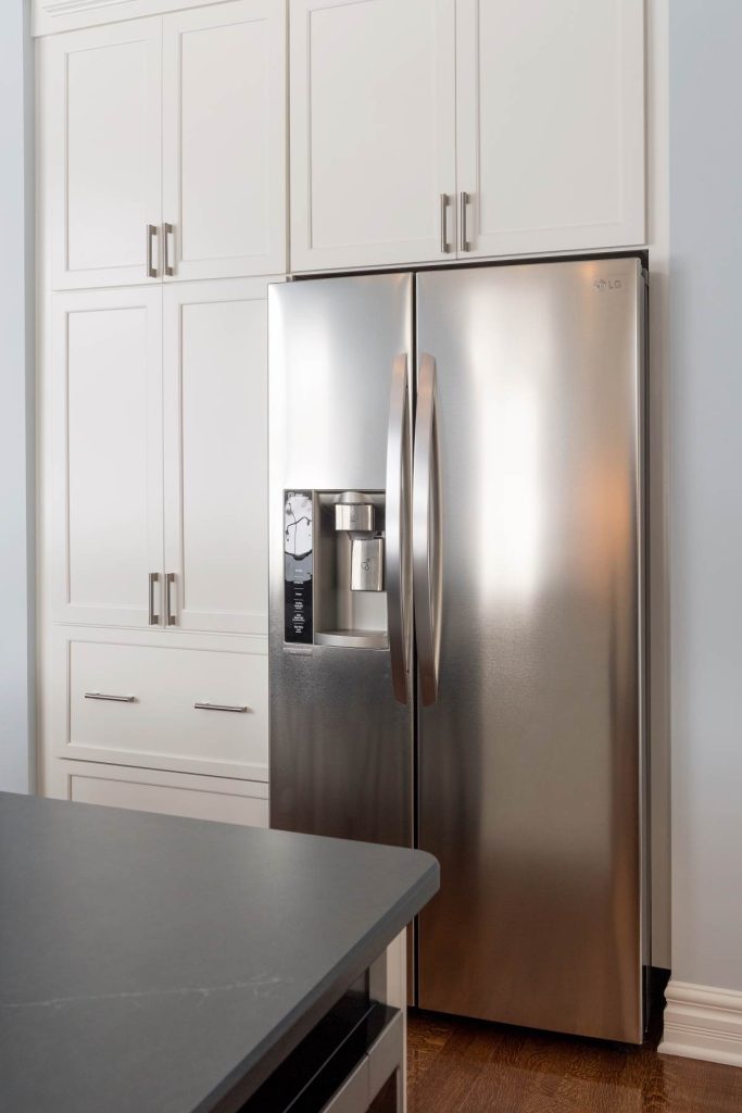 Stainless steel refrigerator surrounded by white cabinets