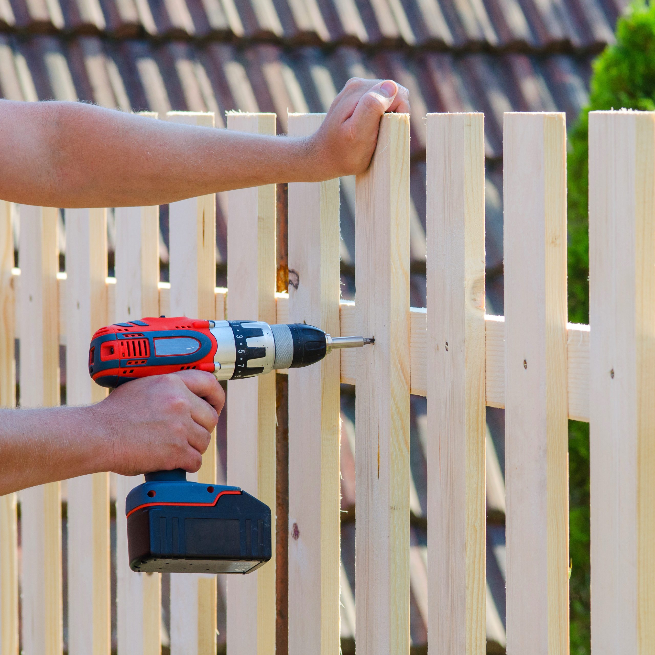 Man hands building wooden fence with a drill and screw. DIY concept. Close up of his hand and tool.